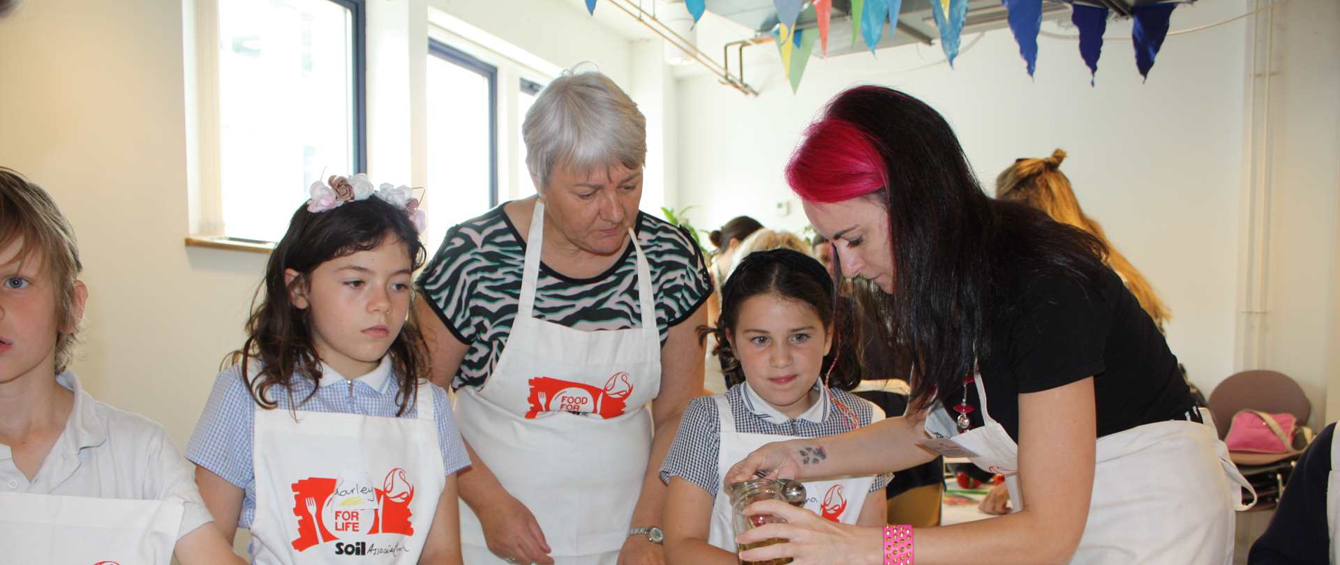Tow adults and three children wearing Food for Life aprons cooking together