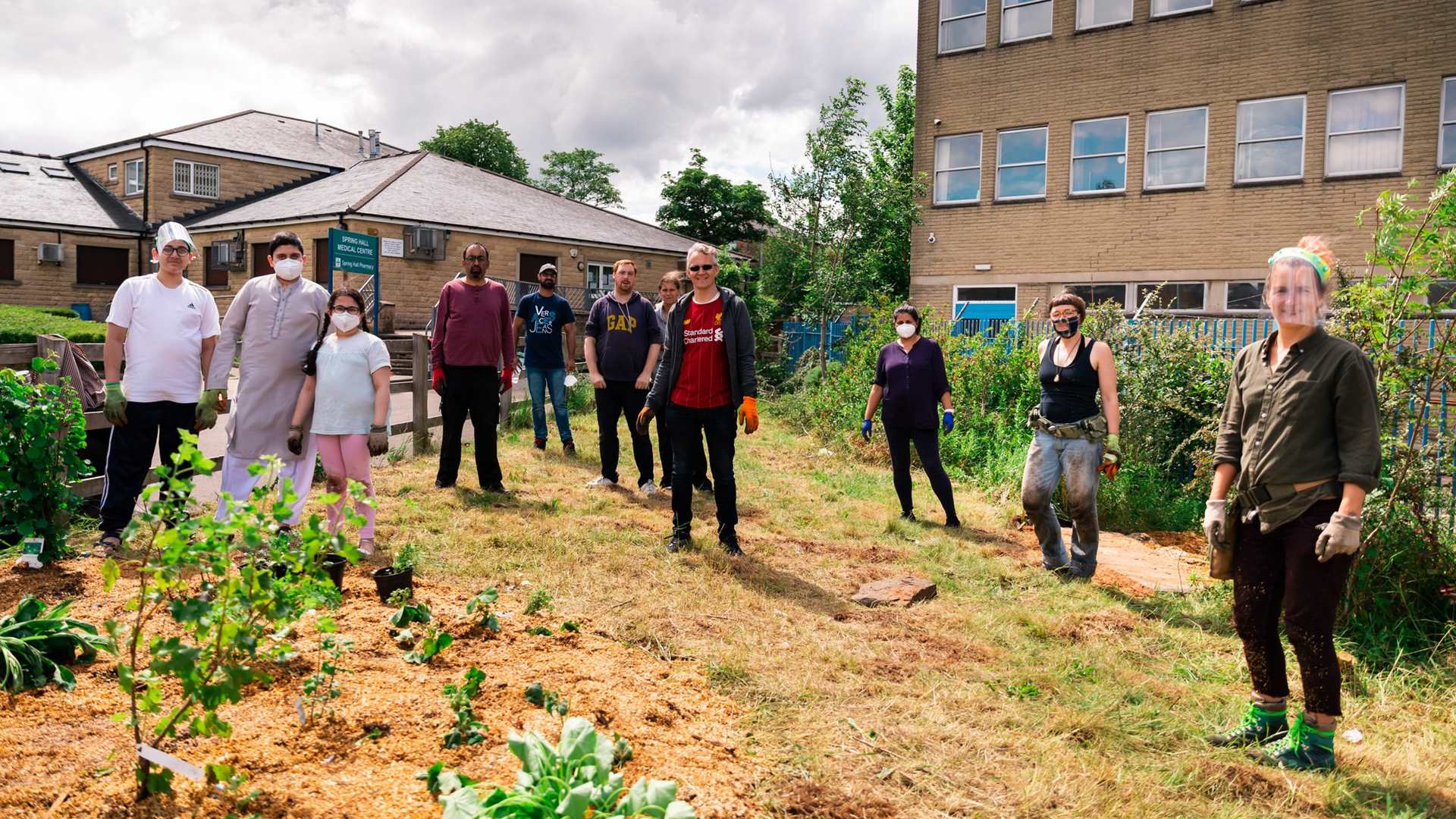 Group of people wearing masks and PPE standing at a distance from one and other in a community garden