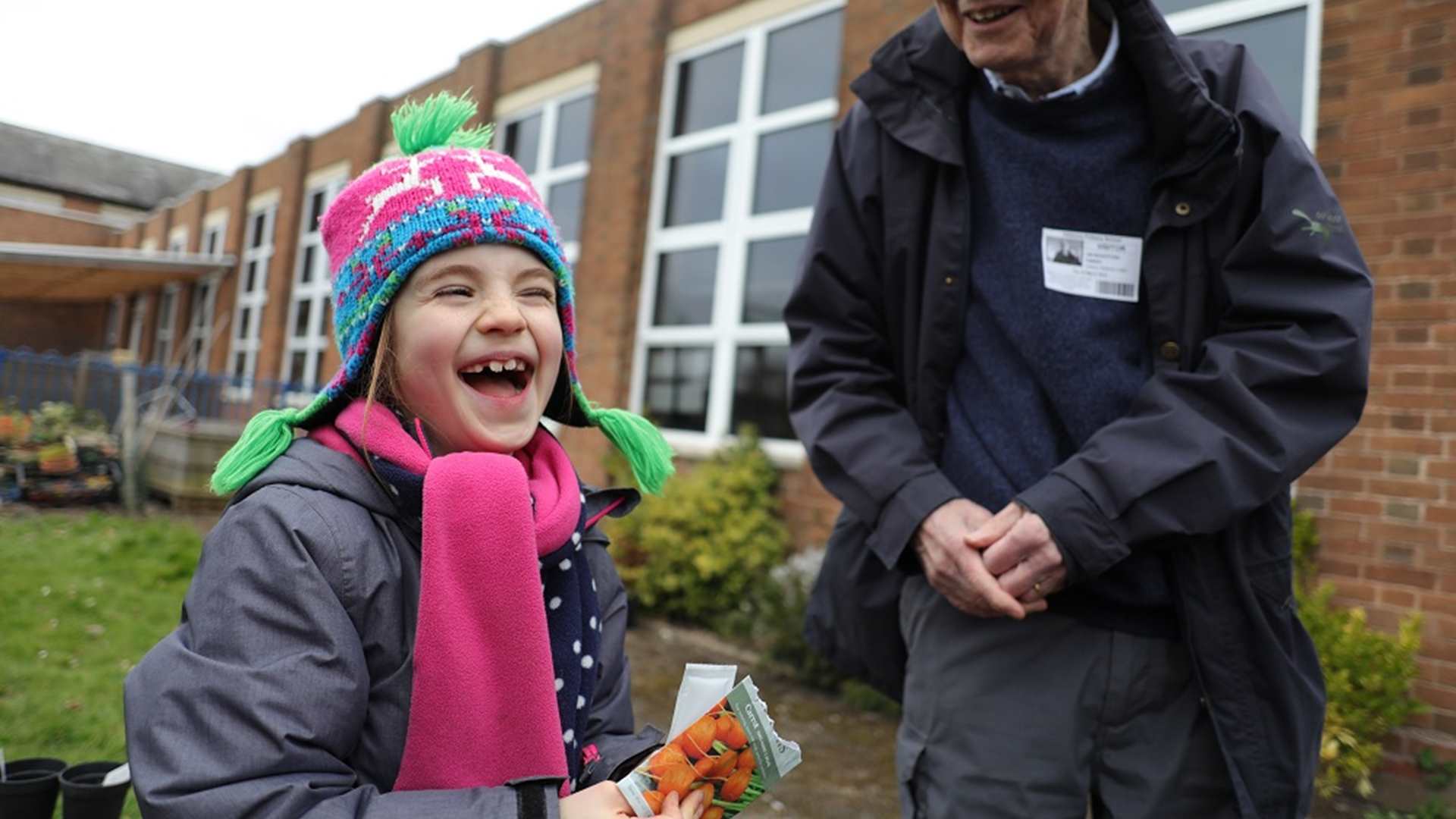 Child laughing with her grandfather while planting carrot seeds