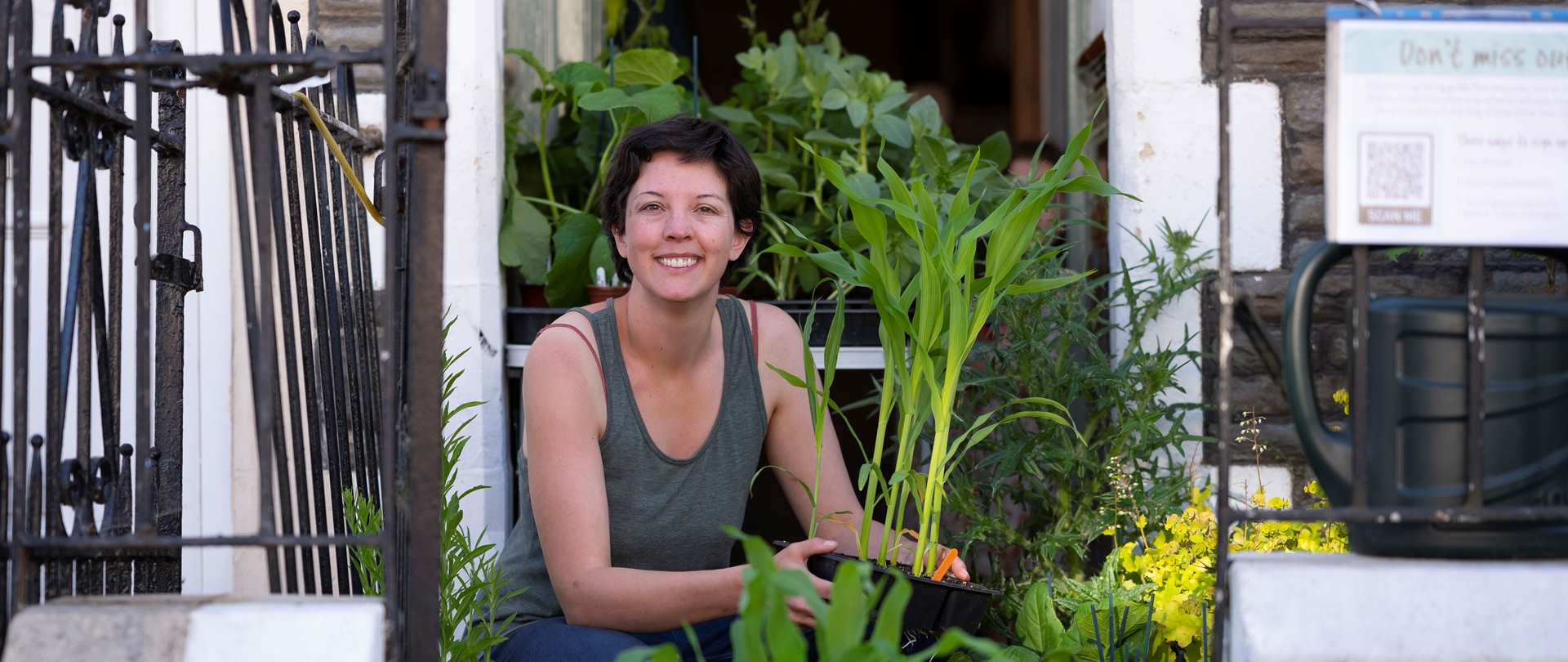 A smiling woman crouching down among plants in pots